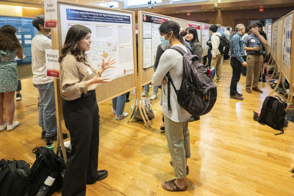 A woman talks to person in front of a poster board.