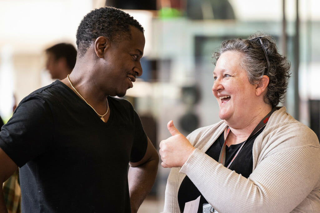 A man and a woman smile at each other, the woman holds up a raised thumb.