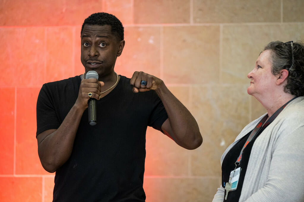 A man talks on stage into a microphone; a woman stands next to him.