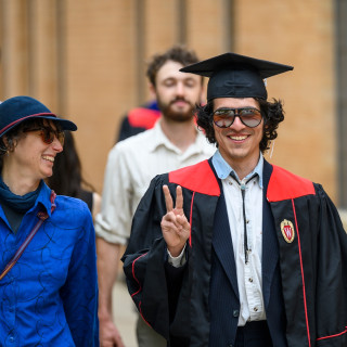 A man in a commencement robe talks with a woman.