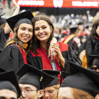 Two women in graduation robes hug and smile.