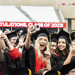 People in commencement robes take selfies, laugh and smile.