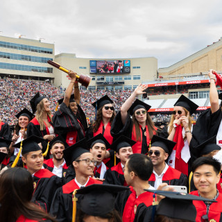 Women in commencement robes smile and hold up a big trophy.