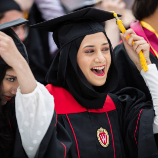 A graduate grabs the tassel on her morterboard cap and moves it.