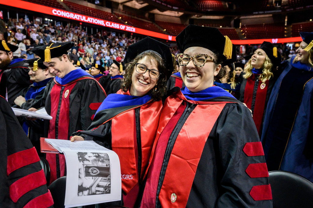 Several people in graduation robes smile and sing.