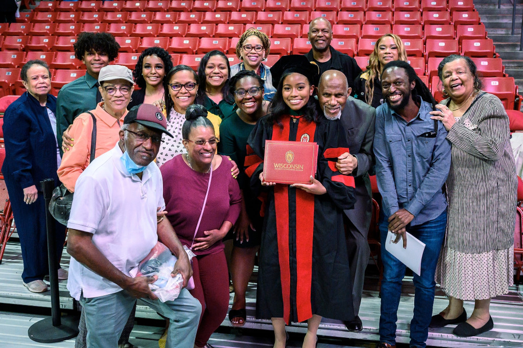 A woman in a graduation gown is surrounded by other people, all smiling for the camera.