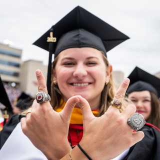 A woman smiles and holds her hands in a W shape; there are three big rings on her fingers.