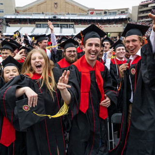 People in commencement robes jump around in the stands.