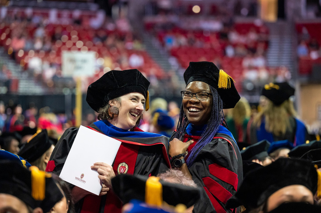 Two women in graduation robes smile happily.