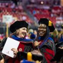 Two women in graduation robes smile happily.