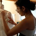 A woman constructs a garment on a sewing form.