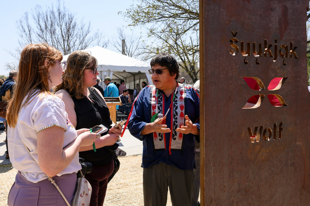 Photo: A man talks to someone in front of a statue.