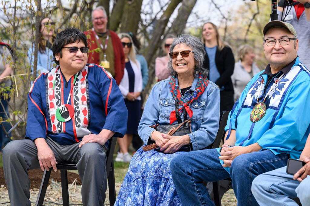 Three people seated alongside each other talk and smile.