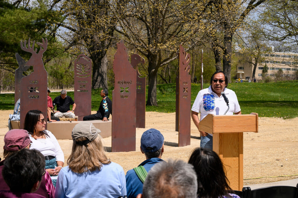 Photo: A man speaks at a podium in an outdoor setting.