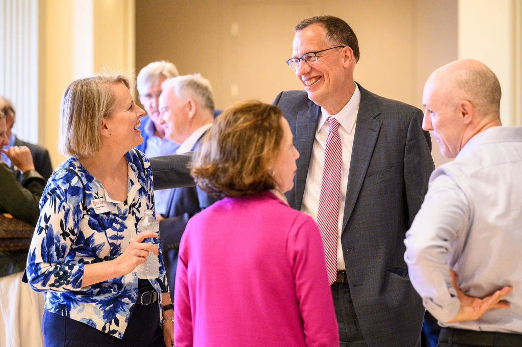 Karl Scholz stands center in a circle with three others having a conversation in a reception setting.