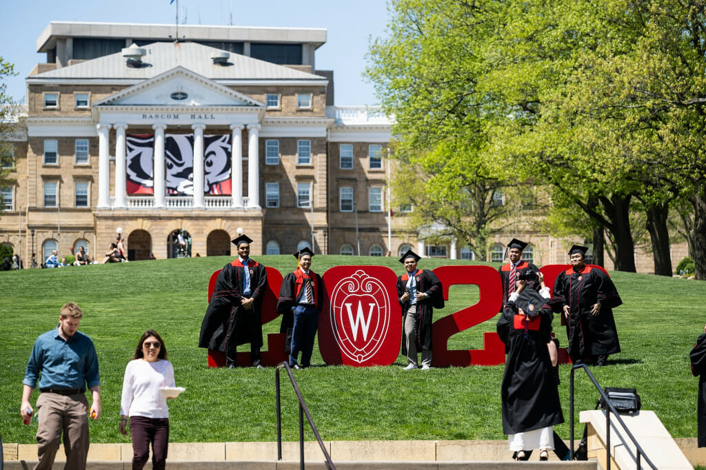 People wearing graduation gowns pose amid big red 2023 numbers on Bascom Hill.