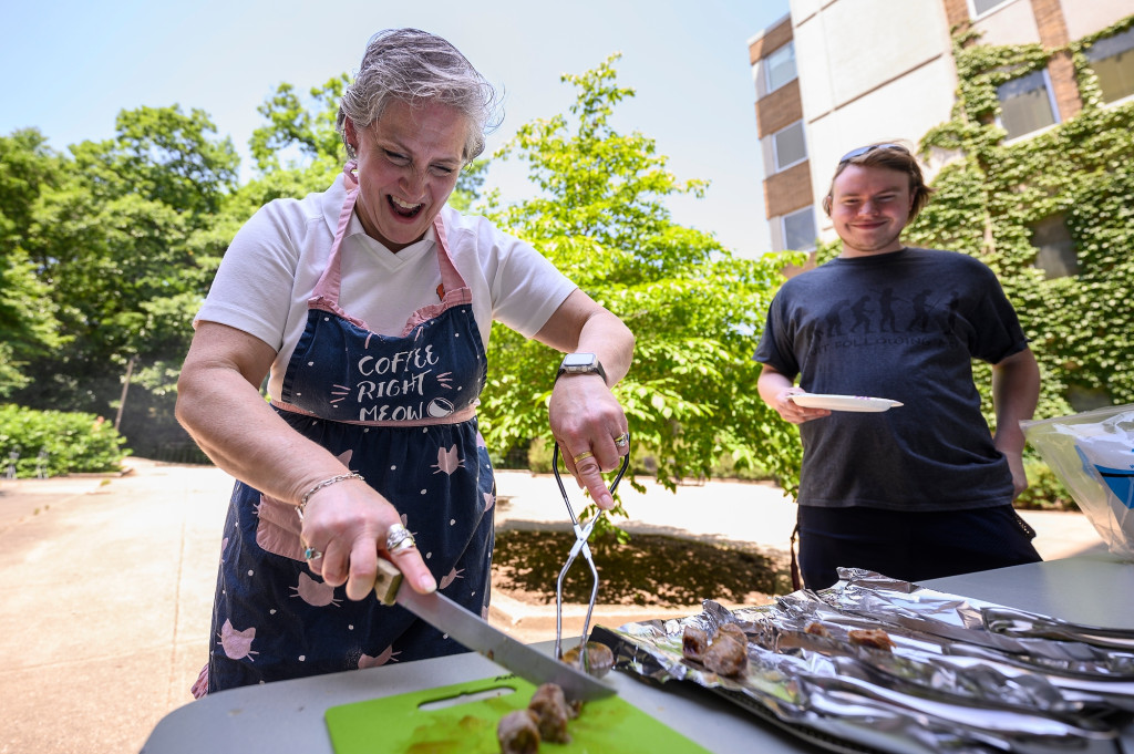 A woman cuts up bratwurst with a knife.