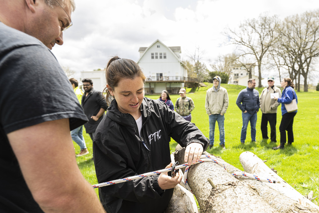 A man and a woman stand by a log and work on tying a rope to it.