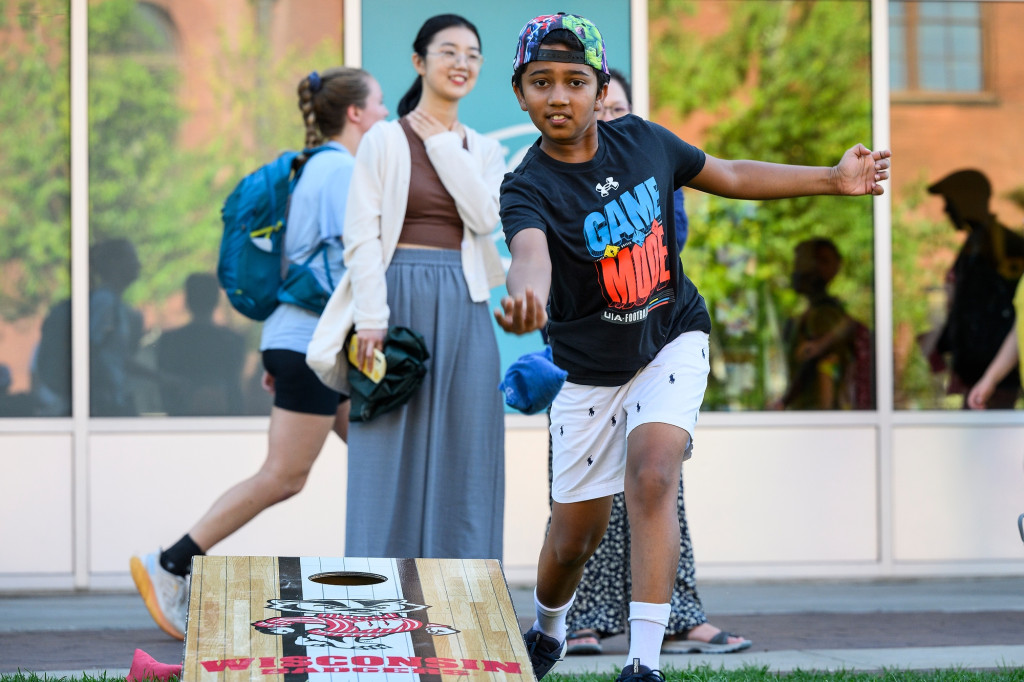 A kid throws a bean bag in a game of corn hole on the lawn in Alumni Park.