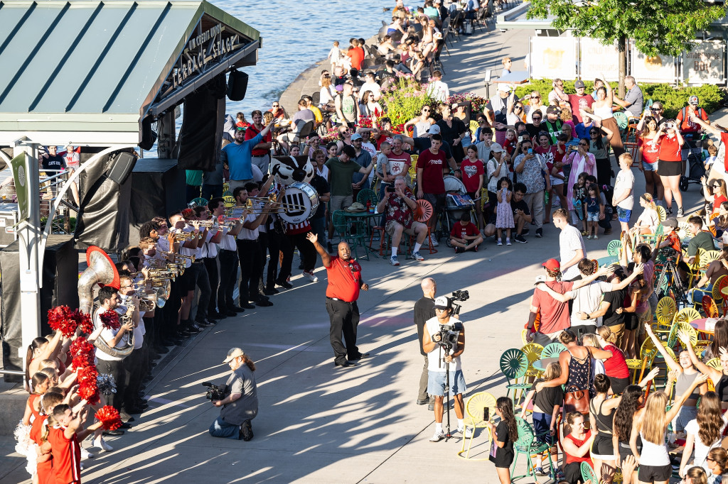 In an aerial shot, band director Corey Pompey waves to the crowd while members of the UW Marching Band play on Memorial Union Terrace.