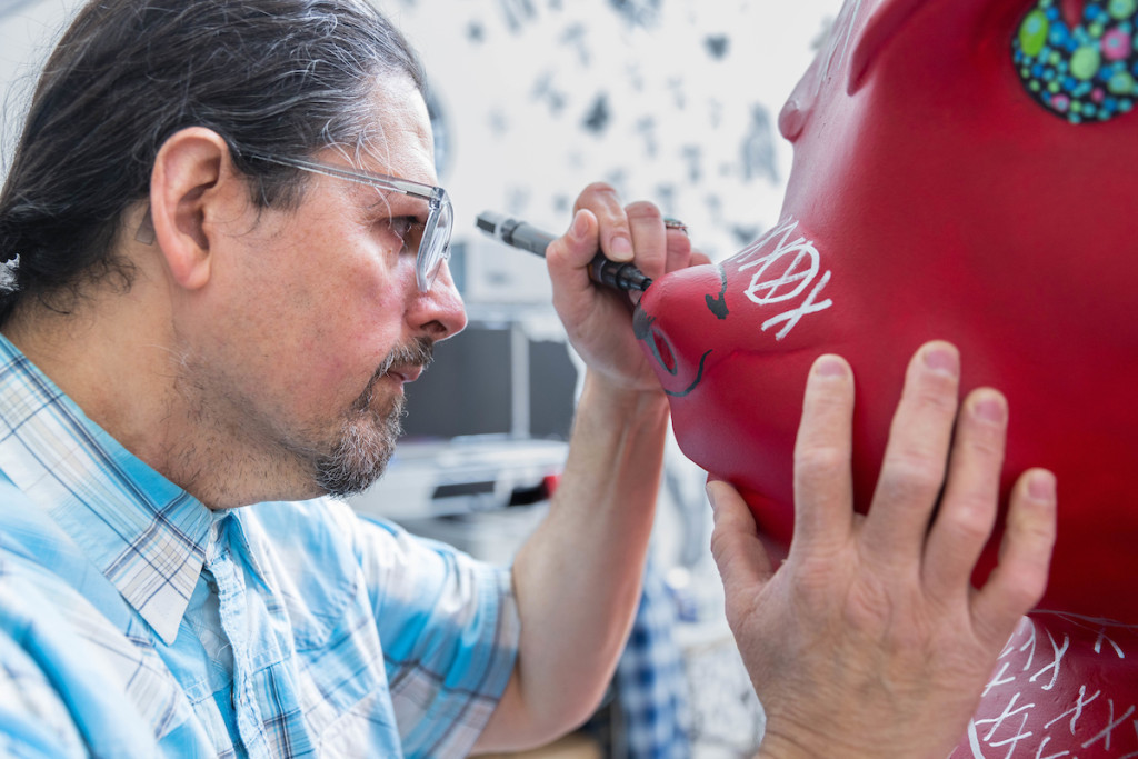 A man stands face-to-face with the Bucky Badger statue as he paints details on it.