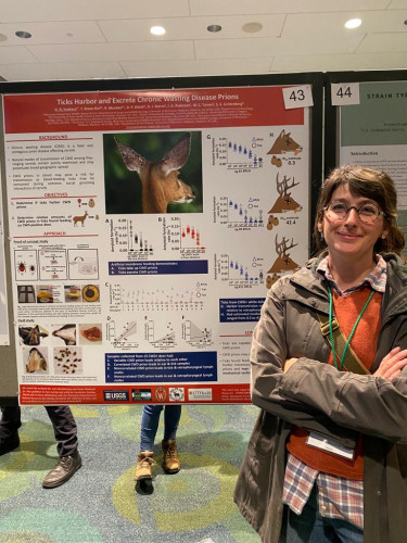 Photo of a woman standing in front of a research poster about ticks, chronic wasting disease and deer.