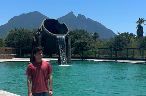 A man stands in front a pool, with mountains in the background.