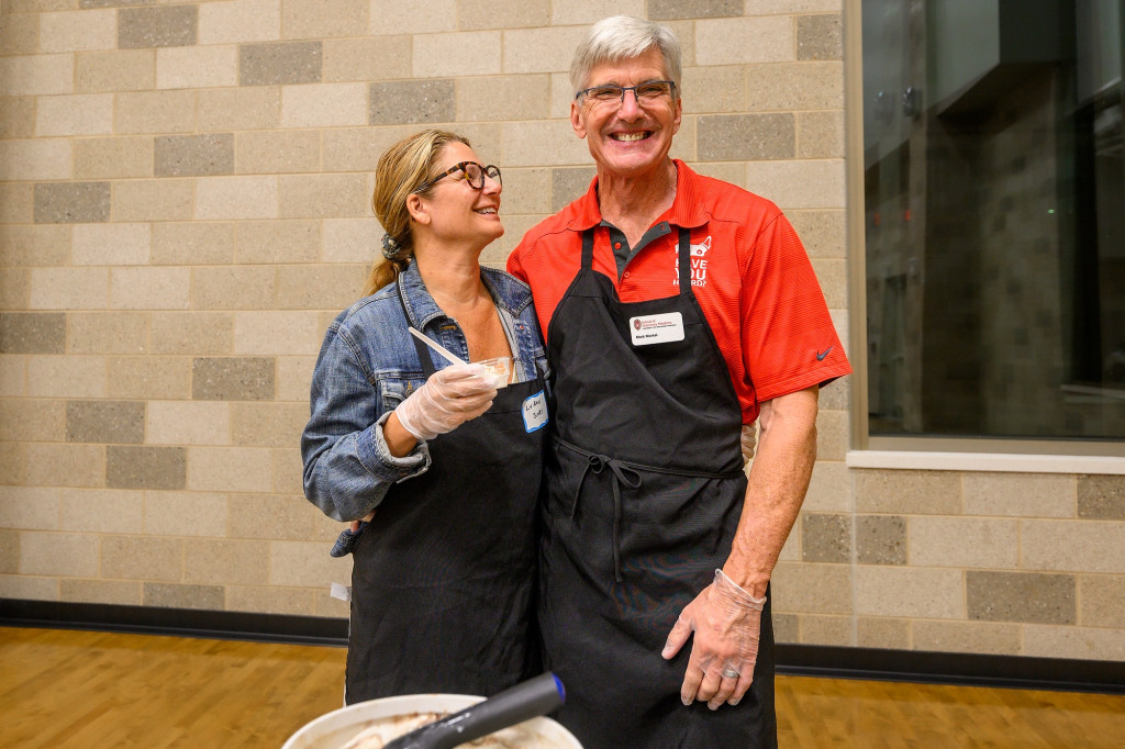 A couple stand arm in arm smiling for the camera.