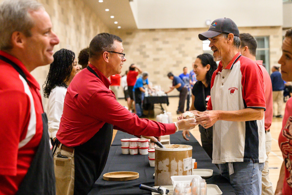 Two men serve ice cream and hand it out to others.