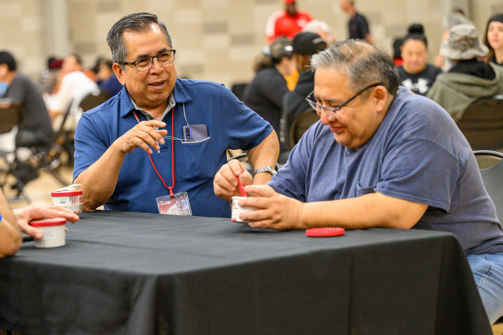 Two men eating ice cream talk while sitting at a table.