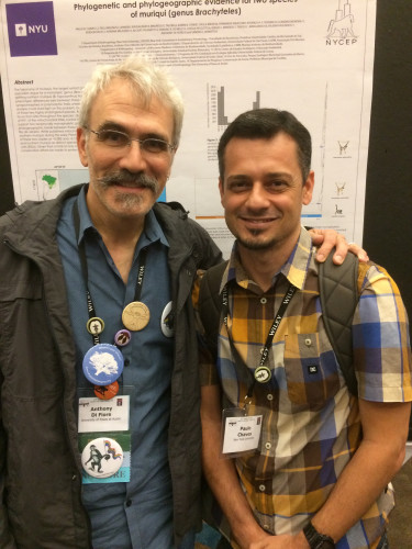 Two men smile as they stand in front of a research poster. The older man has his arm around the shoulder of the younger man as they smile at the camera.