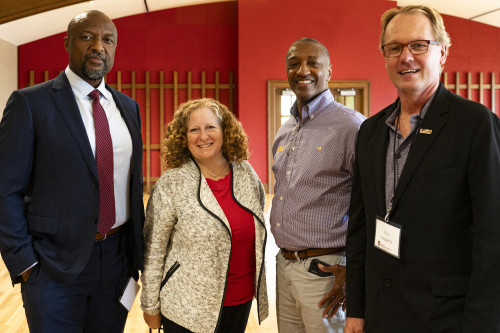 A group of four people in business attire stand together and smile for a photo.