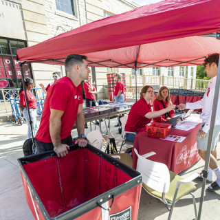 A student talks with people in red shirts outside a residence hall.