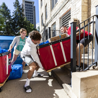 Students work together to lift a heavy red cart up a flight of stairs outside Waters Residence Hall.