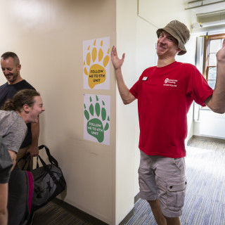 A woman laughs while a man in a red shirt holds his hands up in mock misunderstanding.