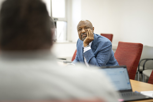 Charles Isbell smiles as he rests his chin on his hand while seated at a conference table.