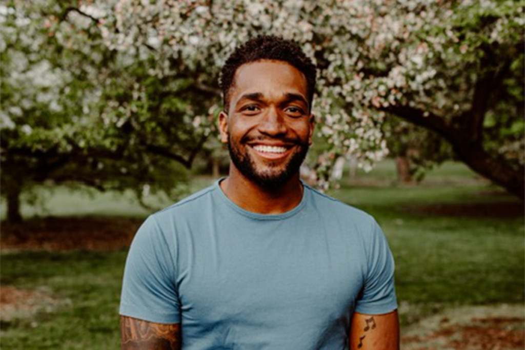 A photo of Quentin Riser smiling to the camera while standing in front of a blooming crabapple tree.