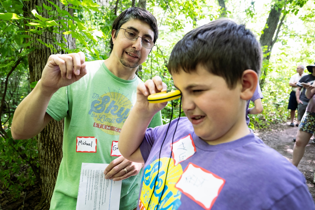 A youth looks through a yellow device as a man helps him.