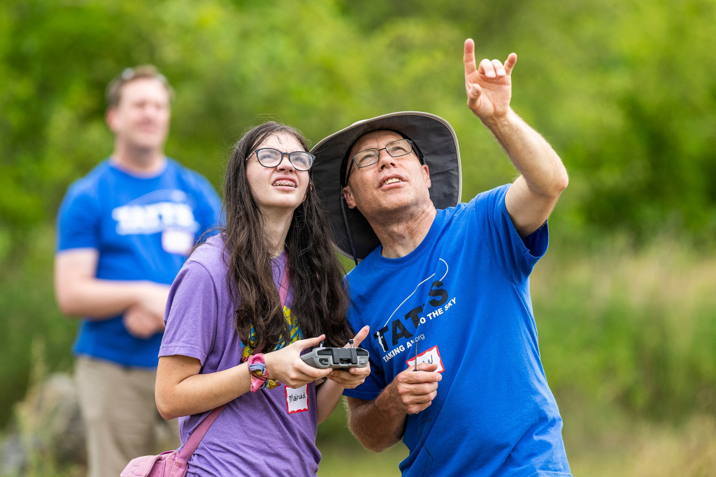 Two people operate a remote control and look up into the sky.