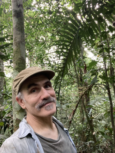 A man takes a selfie while standing under tree canopy in the Brazilian rainforest