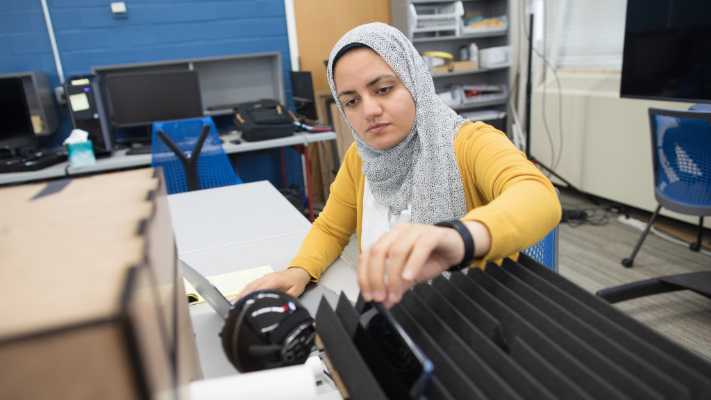 A woman wearing adjusts an iPhone resting on a piece of fsound dampening foam in a lab setting.