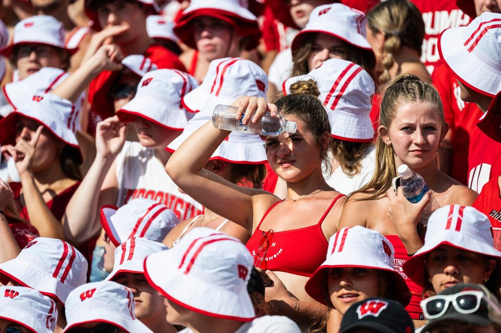 Students in the stands wear white bucket hats, and some have water bottles.