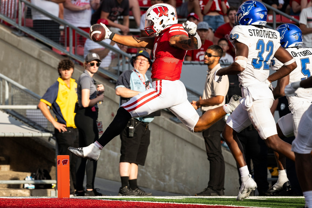 A man in a red football uniform runs as others try to tackle him.