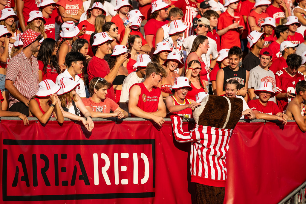 Mascot Bucky Badger exhorts fans in the stands. A sign reads AreaRed.