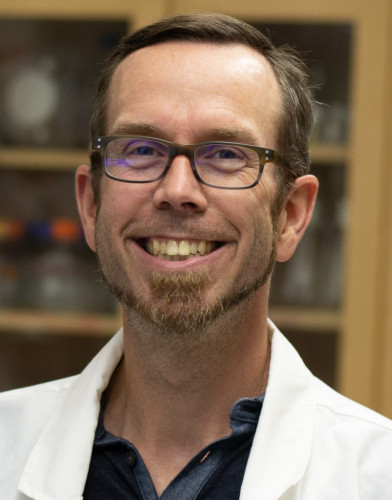 A headshot photo of Andrew Mehle wearing a white lab coat.