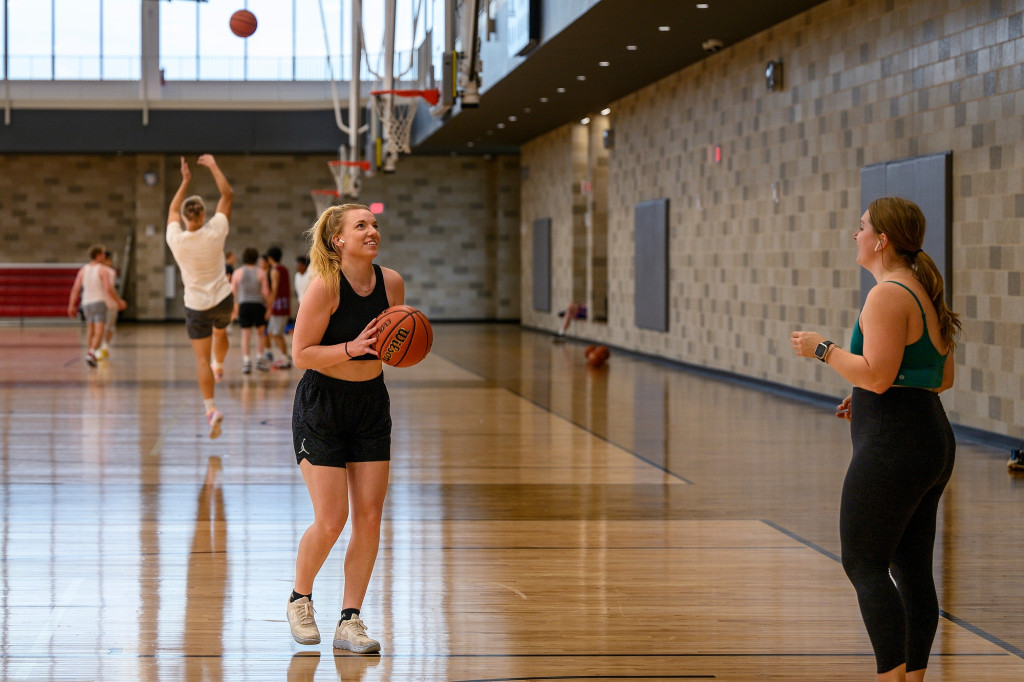 Two women hold basketballs on a basketball courts.