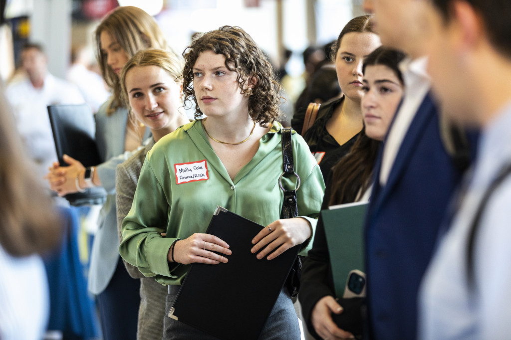 A woman holding papers stands in line.