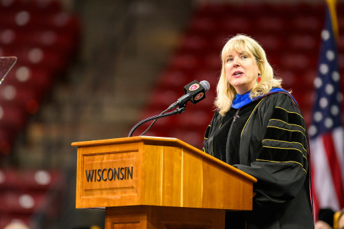 A woman wearing academic robes speaks from a lectern.