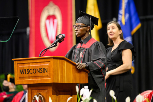 A man speaks from the lectern. He is wearing academic robes.