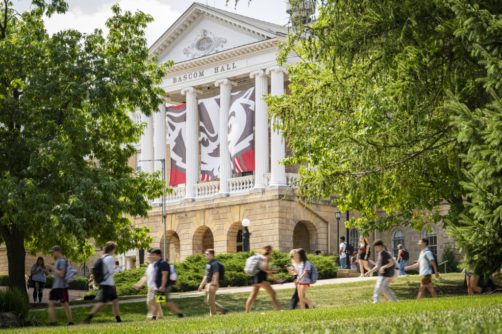 A view of Bascom Hall, a neoclassical building with white columns. Students walk on pathways in front of the building.